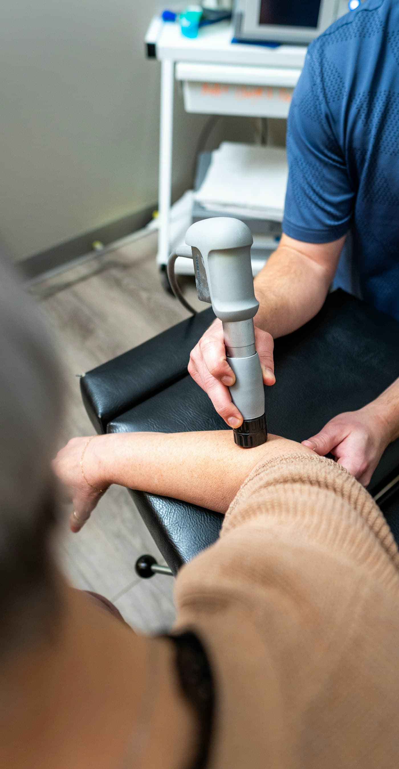 Terapeut care aplică unde de șoc cu un aplicator manual în zona cotului unui pacient
