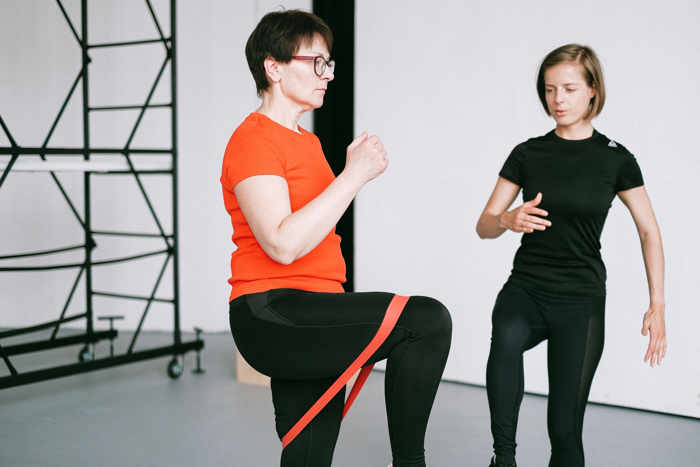 Femeie care execută un exercițiu cu bandă elastică, ghidată de o instructoare