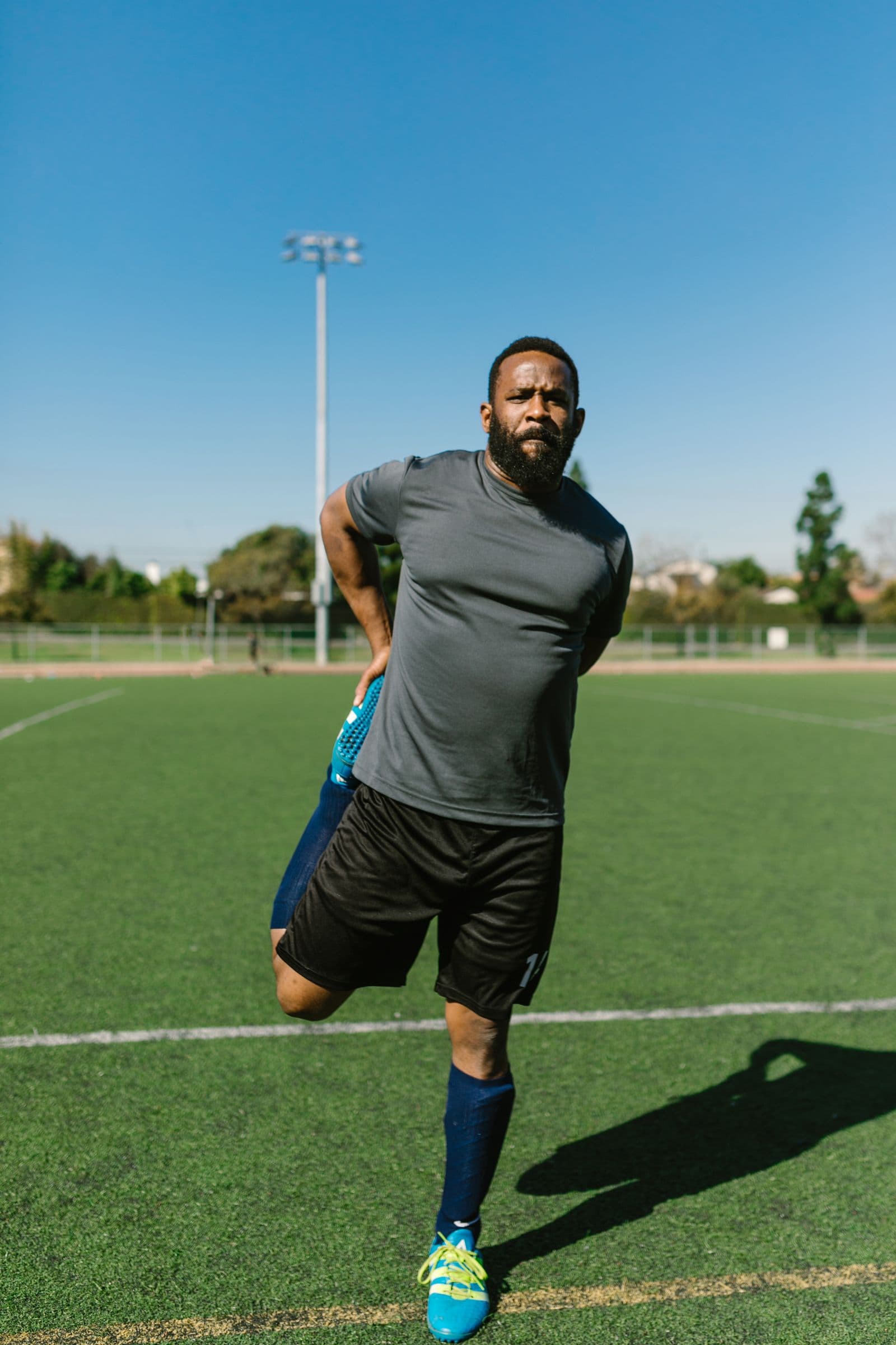 Sportiv care își întinde musculatura coapsei înainte de antrenament, pe teren